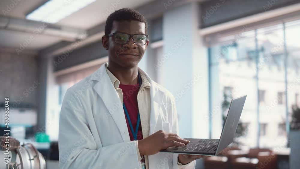 Poster portrait of black young male scientist using laptop computer, looking at camera and smiling in a lab