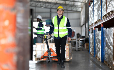 Warehouse worker pulling manual pallet hand truck loaded stack of merchandise in cardboard boxes....