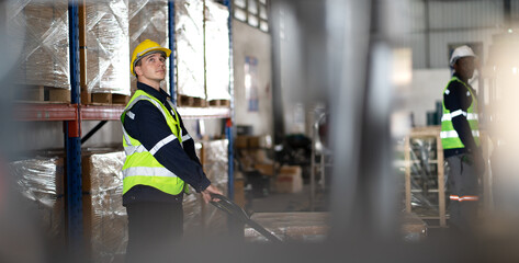 Obraz premium Warehouse worker pulling manual pallet hand truck loaded stack of merchandise in cardboard boxes. Male store worker walking in distribution shipping factory with cargo on hand truck. copy space.