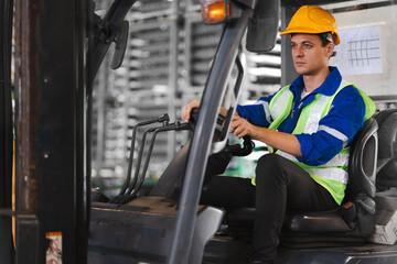 Warehouse worker wears safety helmet driving forklift truck in distribution storehouse. Male vehicle driver working in shipping storage factory lifting, moving and unloading cargo ready for delivery.
