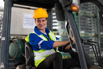 Warehouse worker wears safety helmet driving forklift truck in distribution storehouse. Male vehicle driver working in shipping storage factory lifting, moving and unloading cargo ready for delivery.