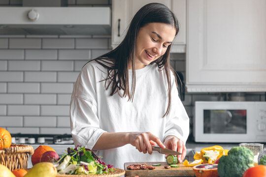 Attractive young woman cutting vegetables for salad in the kitchen.