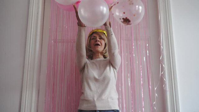 Mature woman with crown golden balloon, fringe party curtain and balloons. Celebrating event