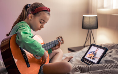 Little girl learns to play the guitar, online music video lesson.