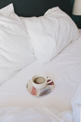 Cup of coffee on a white bed in a hotel room.