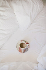 Cup of coffee on a white bed in a hotel room.