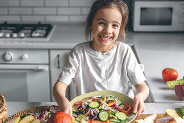 Little girl holding a plate with fresh vegetable salad, healthy eating concept.