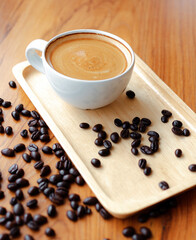 White cup of espresso coffee and Roasted coffee beans on wooden counter at coffee shop