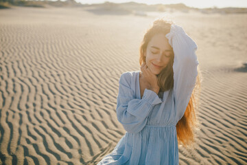 Woman with long hair in a stylish dress poses in the desert sands.