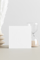 Square invitation card mockup with a pampas decoration on the beige table.
