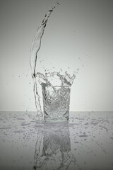 Vertical shot of crystal water glass with water splash and droplets around, on a white shiny table