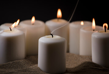 Fototapeta na wymiar Wax and smoke candle, surrounded by candles with a burning flame, in the sand