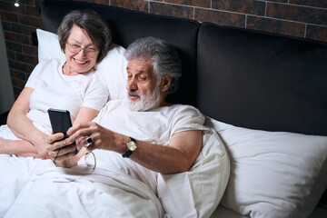 Happy old couple resting in bed, chatting with family