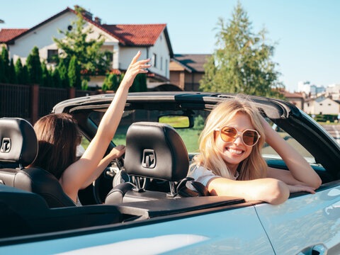 Portrait of two young beautiful and smiling hipster female in convertible car. Sexy carefree women driving. Positive models riding and having fun in sunglasses outdoors. Enjoying summer days