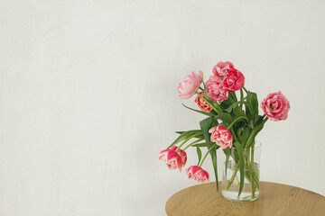 Stylish beautiful pink tulips bouquet in vase on wooden table in rustic room. Floral arrangement in...