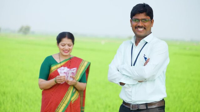 rack focus shot of Happy banker standing with crossed arms in front of woman counting money by looking at camera at farmland - concept of financial or banking support, aspirations and belief.