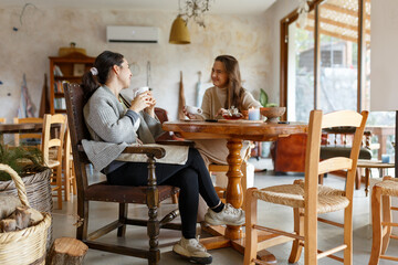 Fototapeta premium Two woman friends drinkind coffee or tea together. Talking, laughing and enjoying their time. Lifestyle and friendship concepts with real people