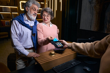 Elderly man and woman leaving hotel and paying their stay