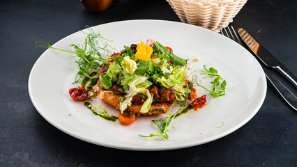Fresh salad with fried chicken, lettuce, tomatoes, greens and sauce on a dark table.