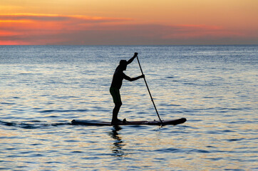 Silhouette of man is rowing on a SUP board against background of sunset sky. Standing paddleboarding