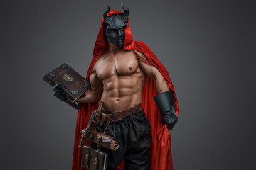 Fototapeta na wymiar Studio shot of handsome fanatic of dark cult dressed in horned mask and red cloak.