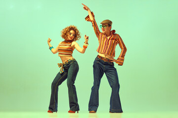 Two excited people, man and woman in retro style clothes dancing disco dance over green background. 1970s, 1980s fashion, music, hippie lifestyle, - obrazy, fototapety, plakaty