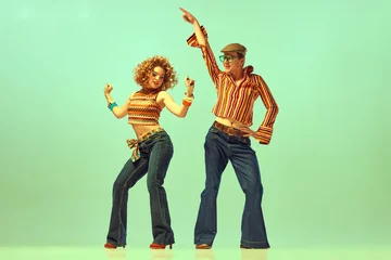 Poster Two excited people, man and woman in retro style clothes dancing disco dance over green background. 1970s, 1980s fashion, music, hippie lifestyle, © Lustre