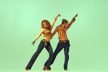 Two excited people, man and woman in retro style clothes dancing disco dance over green background....