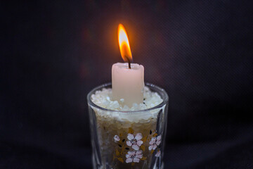 A burning candle in a glass of rice stands on a black background	
