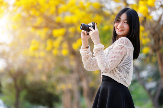 Portrait cute smiles Asian of attractive young teenage girl a holding the camera in blooming Yellow Golden Tabebuia Chrysotricha flowers with the park in spring day at Evening background in Thailand.