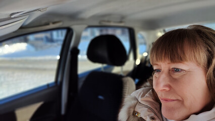 Woman sitting in the car in the road trip. Blonde senior Woman driving transport. Lady travelling in cold time