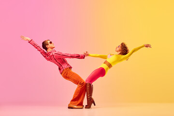 Young stylish emotional man and woman, professional dancers in retro style clothes dancing disco dance over pink-yellow background. 1970s, 1980s fashion, music concept - obrazy, fototapety, plakaty