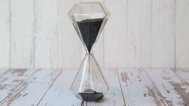 Black sand spills over in an hourglass glass transparent
