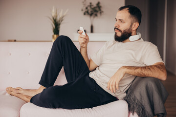 Man uses the remote control to use the neck massager device sitting on a sofa at home