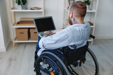 A man in a wheelchair freelancer works at a laptop at home, restriction of movement, view from the...