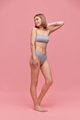 Fototapeta na wymiar Beautiful slender young woman wearing grey cotton inner wear posing over pink background. Concept of natural beauty, body and skin care, healthy eating