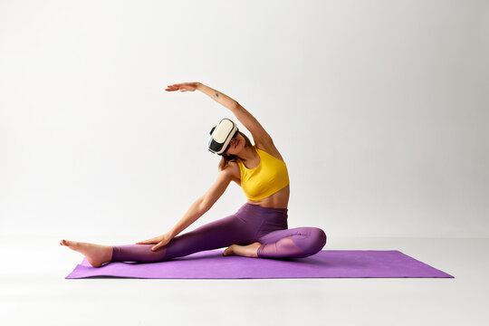 Stretching. Flexible sportive young girl doing yoga exercises in VR headset glasses. Concept of sport, health and virtual reality
