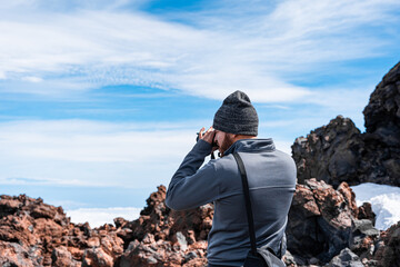 Joven hombre turista con ropa de invierno fotografiando paisaje rocoso con vistas increíbles del horizonte con cielo azul y algunas nubes a más de 2000 metros, vistas desde el teide