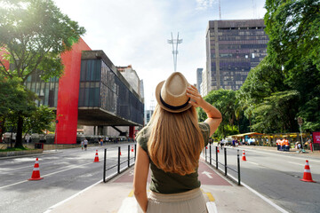 Visiting Sao Paulo City, Brazil. Rear view of beautiful tourist woman with hat walking along...