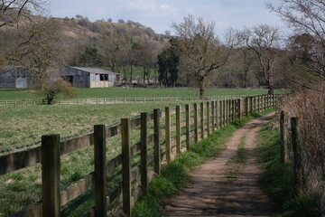 farm track road by a field and a barn surrounded by wooden fence