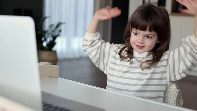 Cute little girl preschooler doing an online finger gymnastics looking at the screen of laptop