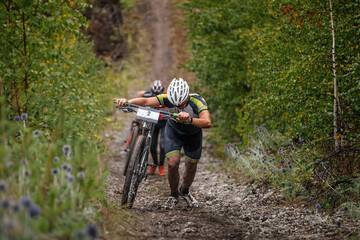 Fototapeta two cyclists go uphill with their mountain bike. heavy climb on muddy slope. cross-country cycling competition obraz