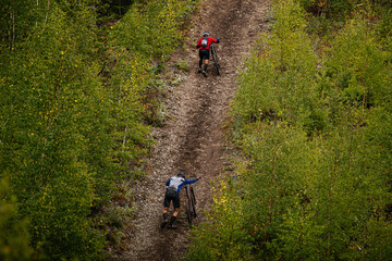 back two cyclists climb uphill with mountain bike in trail forest. cross-country cycling competition