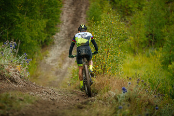Obraz na płótnie Canvas back male athlete on mountain bike ride forest trail. dirt on feet and body. cross-country cycling competition