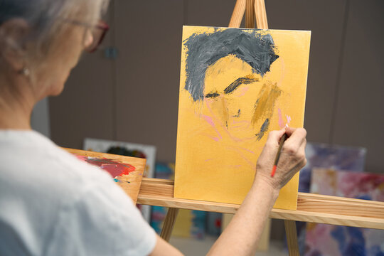 Gray-haired woman paints a portrait with paints and brush