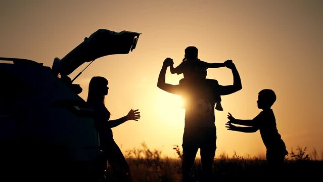 Road trip. Dad holds his daughter on his neck and shoulders. Silhouette of car in nature in park. Family picnic in spring in park. Son and mother play with ball in park. happy family dream at sunset