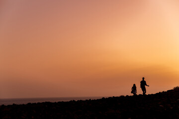 Fototapeta na wymiar Silhouettes of a couple, tall man and short man, walking across rocky landscape with a deep red sunset on Tenerife Canary Islands