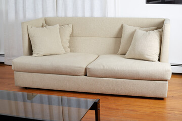White textured Modern remake of a mid-century modern design sofa. Couch with nubby, soft, and subtle herringbone fabric covers. Interior view with long white curtains and glass-top coffee table. 