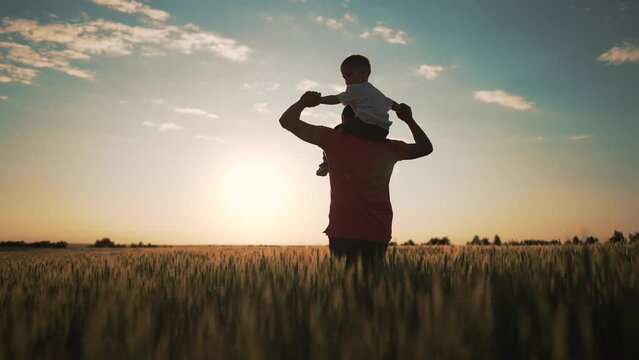 Happy family. Father Day.Baby sits on father neck.Boy on his father shoulder play in nature in field.Family of farmer in wheat field at sunset.Child pilot of aircraft on neck of father shoulders