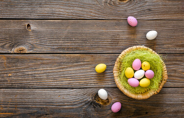Easter eggs in a decorative nest on a wooden background, top view.
